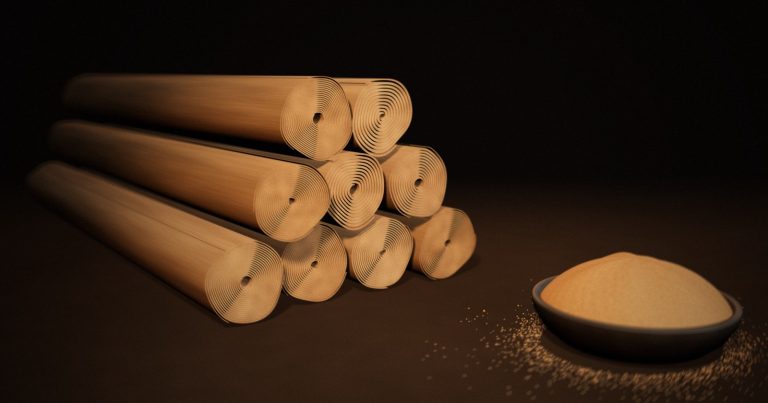 Stacked Ceylon cinnamon quills showing their thin rolled layers, beside a bowl of ground Ceylon cinnamon